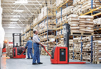 Man pulling pallet jack while retrieving pallets from racks in warehouse