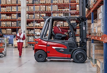 Preview image Woman walks past behind Linde forklift truck in warehouse